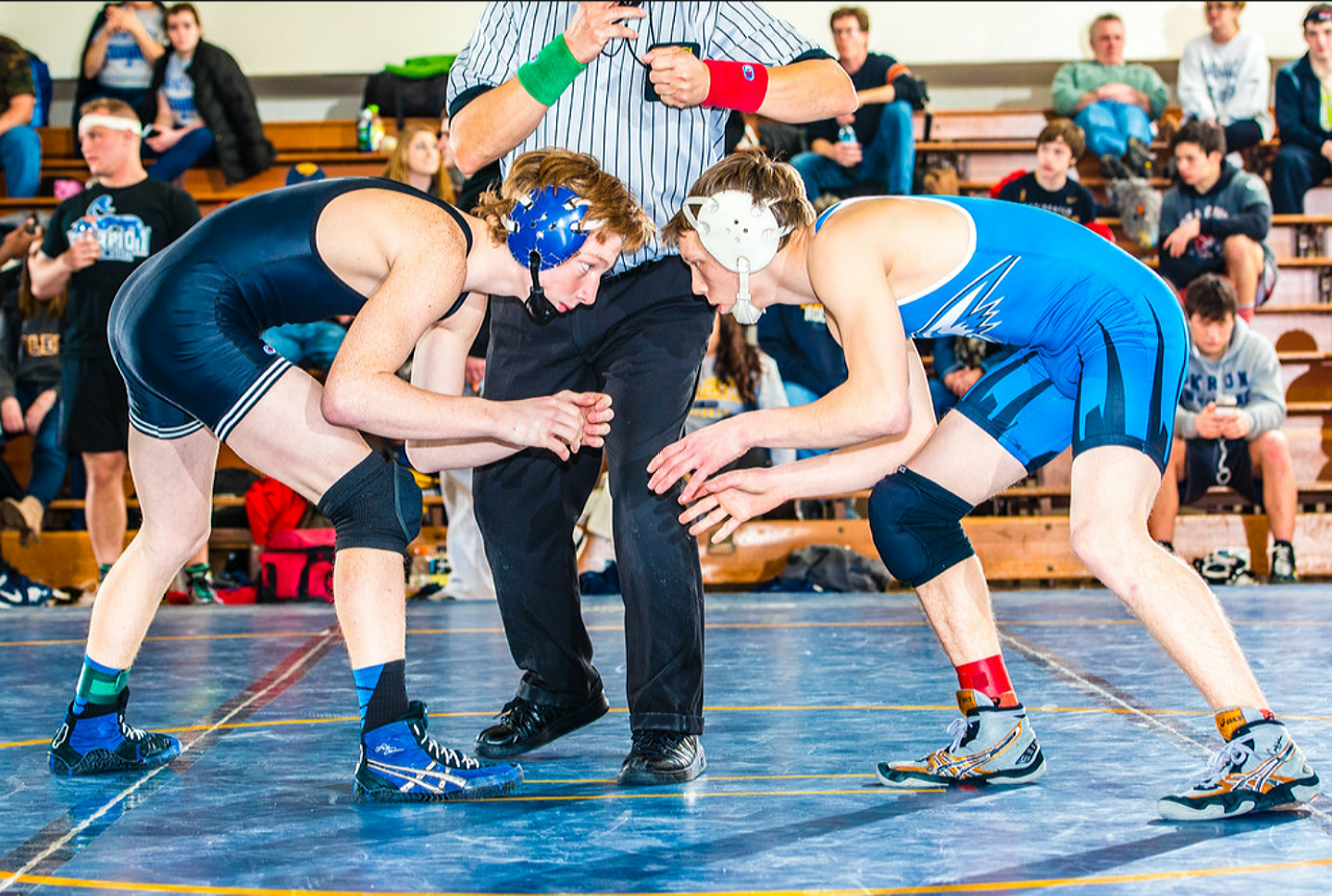 Two wrestlers crouch in ready position, a referee positioned next to them.