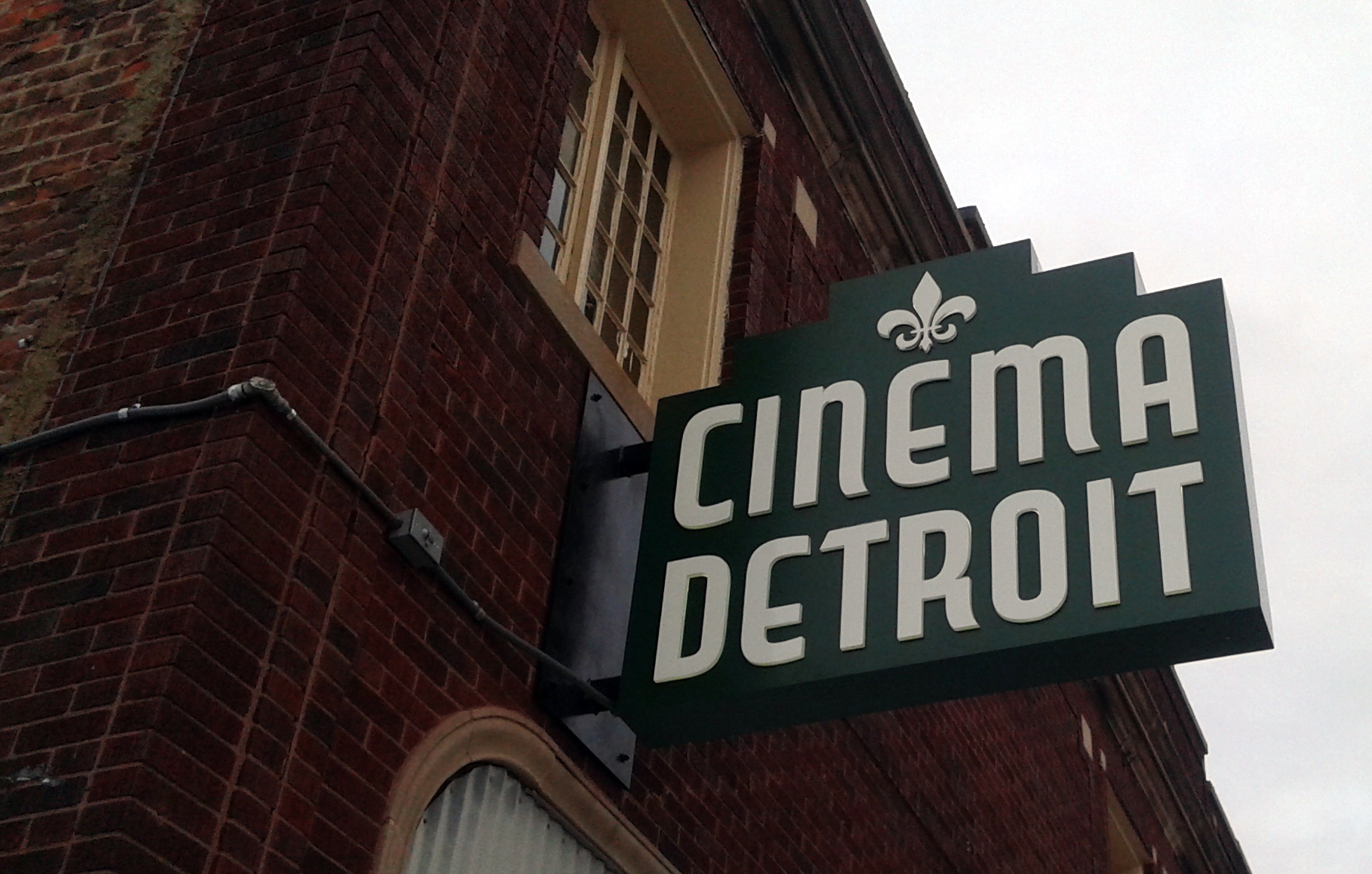 A building made from red brick holds the sign for Cinema Detroit. Their sign has a fleur-de-lis at the top.