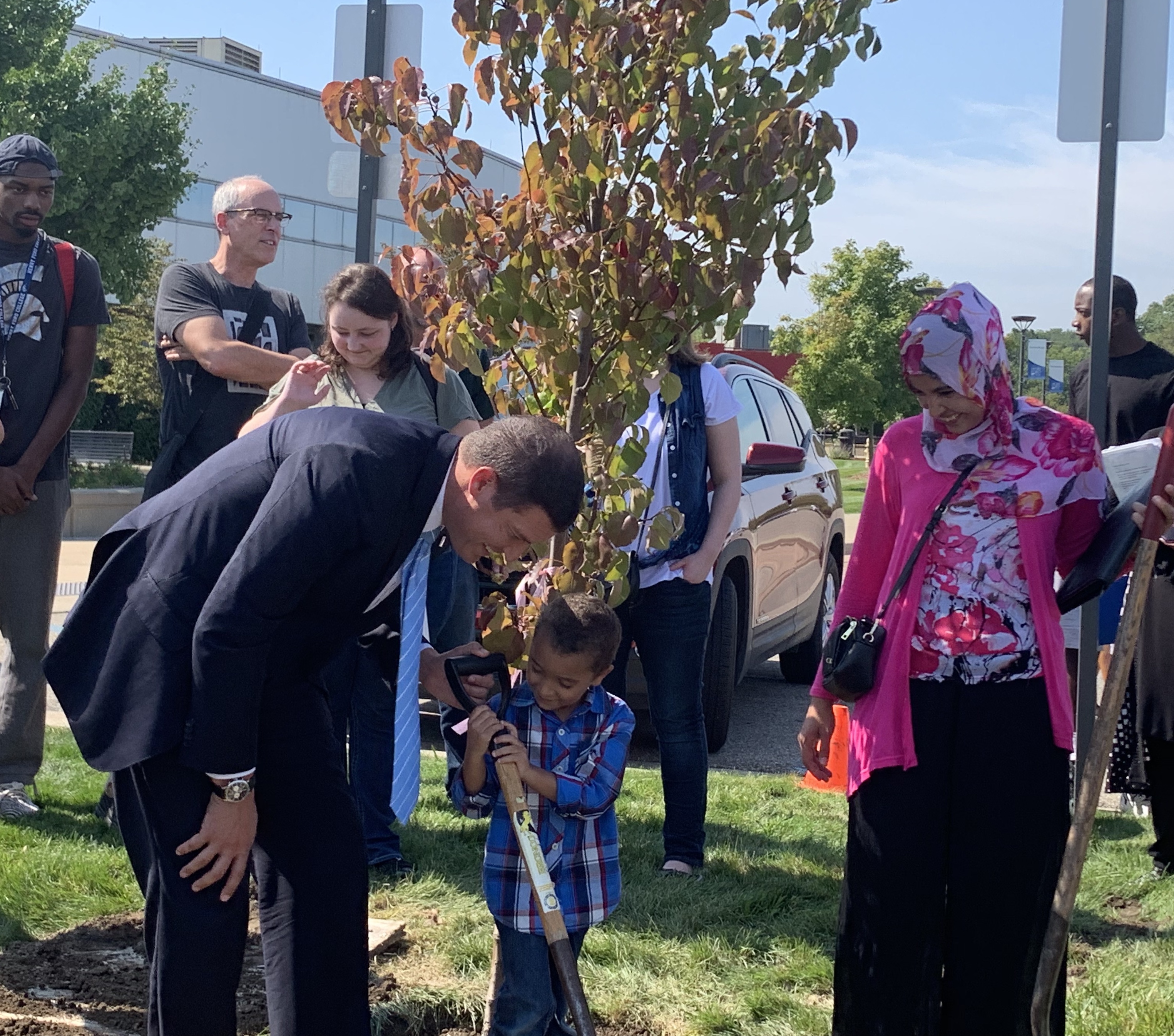 Photo of HFC President Russell Kavalhuna planting a tree with a student and her young child