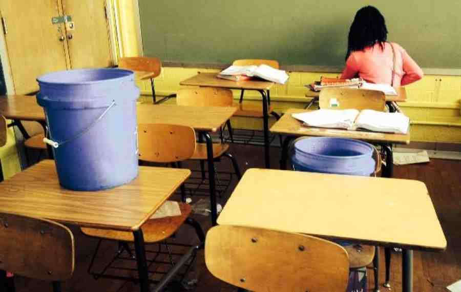 Buckets on desks catching leaks in a public school classroom