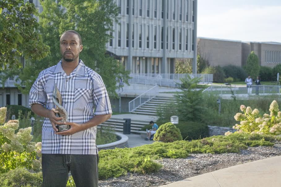 Shahid Mohammad standing in front of the Liberal Arts building holding his film award.