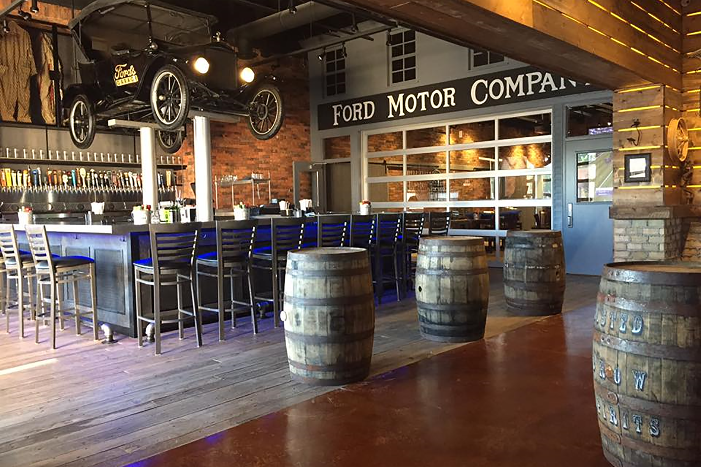 Ford's Garage interior having an old car hanged in the ceiling above chair and tables.