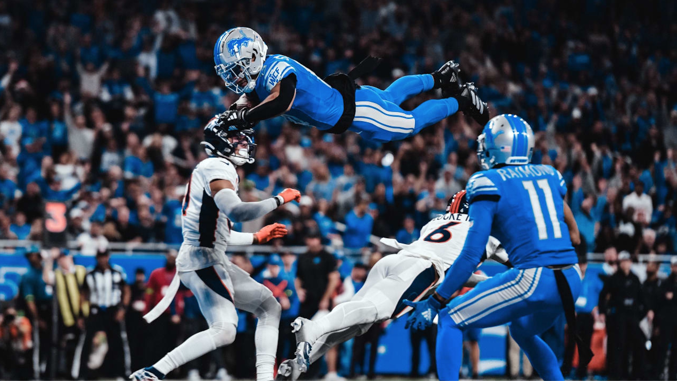 Photo of Lions receiver Amon-Ra St. Brown jumping over Broncos defenders for a touchdown courtesy Detroit Lions