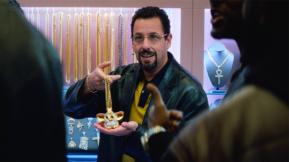 Still image from "Uncut Gems" showing Adam Sandler holding a Furby gold chain