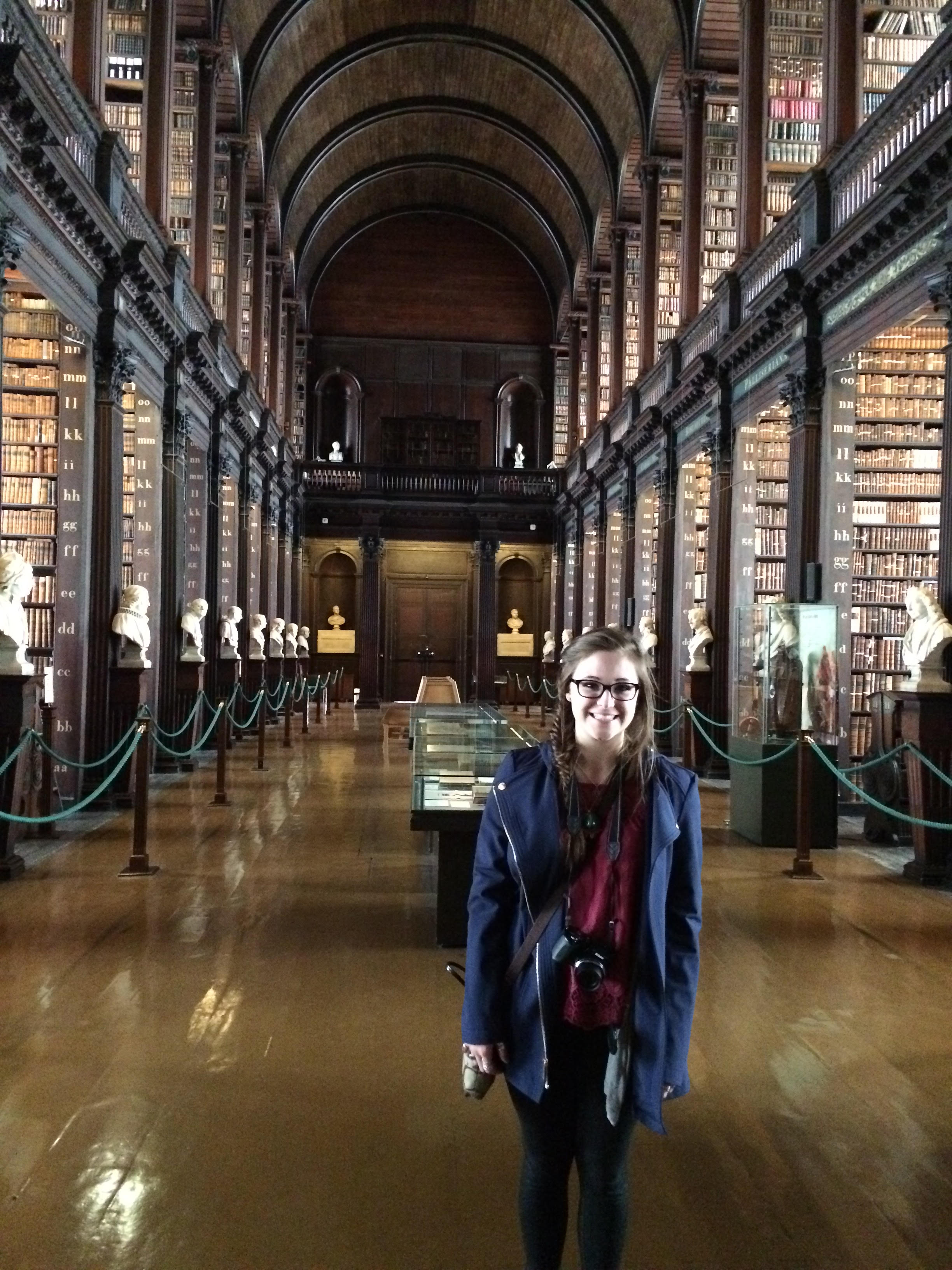 Photo of Sophia Hart standing on the main floor of the Old Library at Trinity College with its historic high vaulted ceilings.
