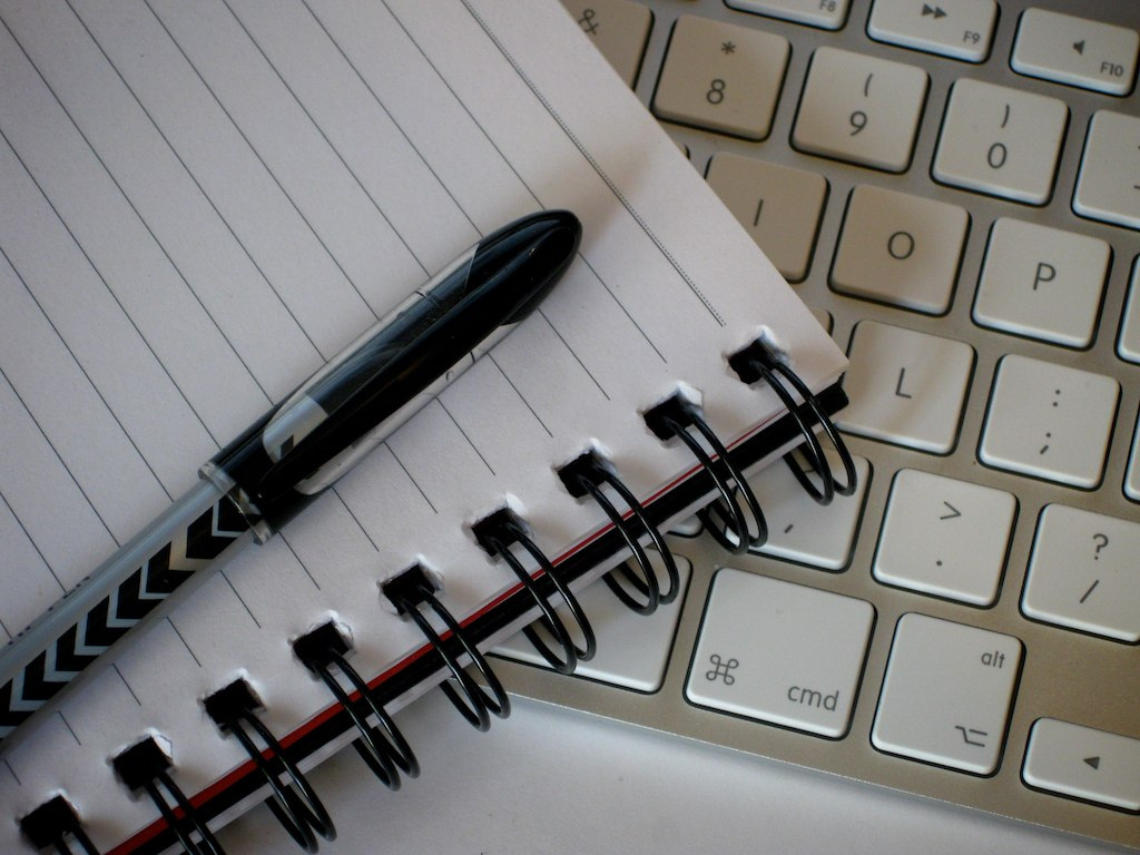 Photo of writing pad, pen, and computer keyboard.
