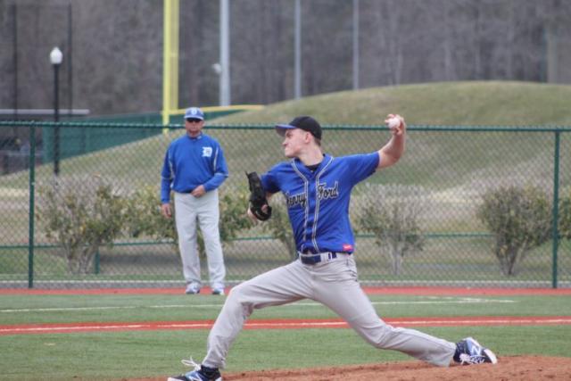 A pitcher is midthrow from the pitcher's mound, while a coach looks on.