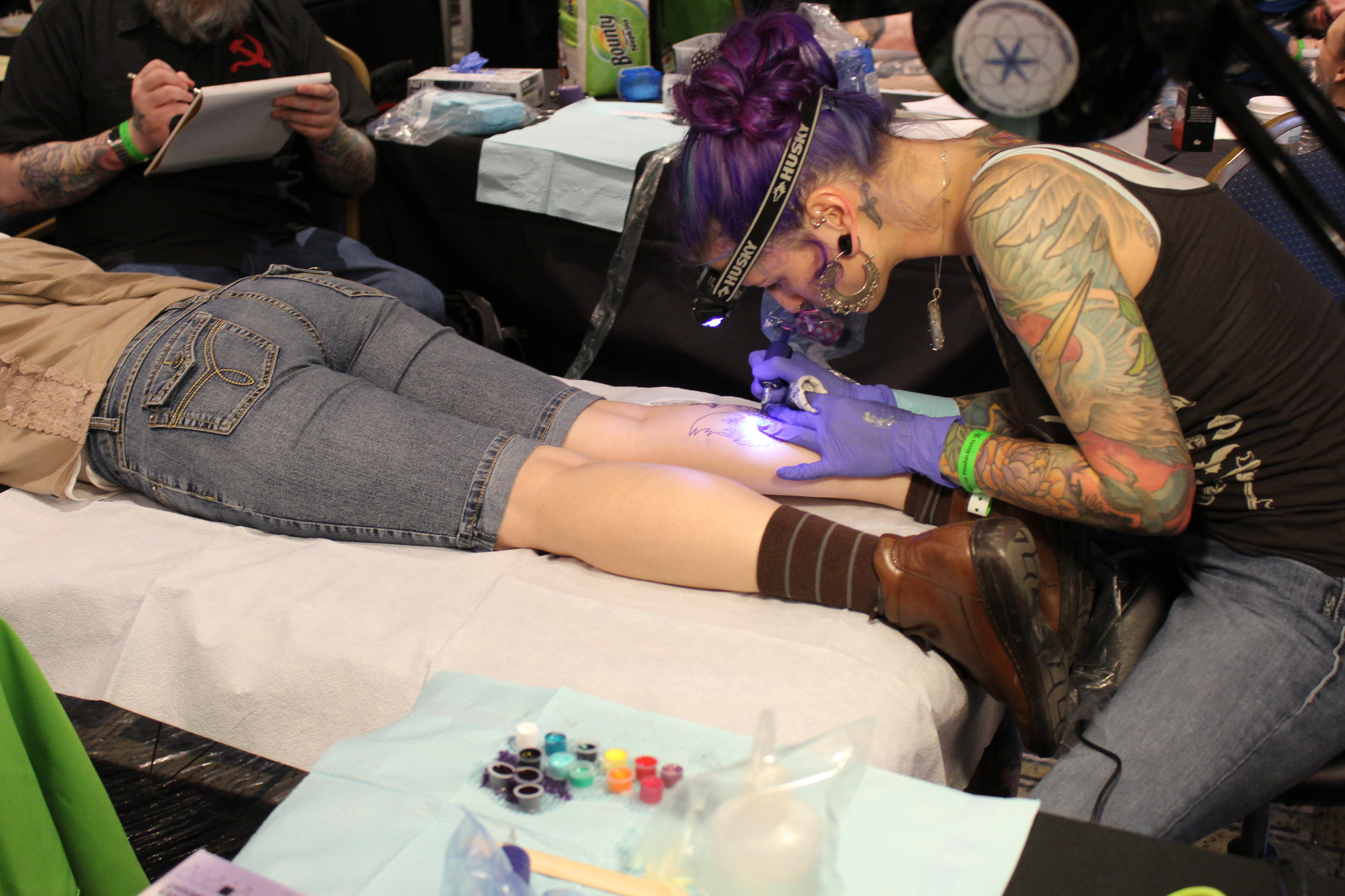 A tattoo artist works on a tattoo on the back of someone's calf area.