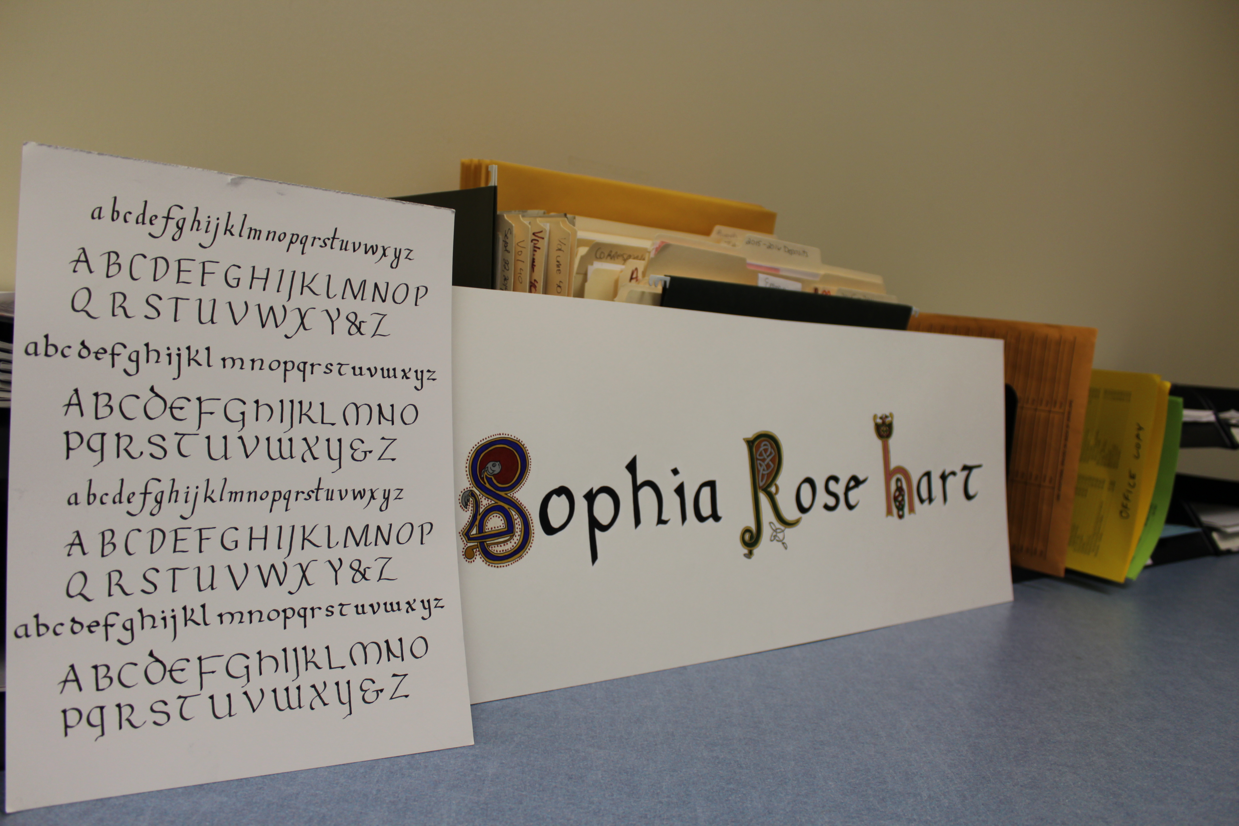 Calligraphy of Sophia Rose Hart next to a sheet with several calligraphy letters.