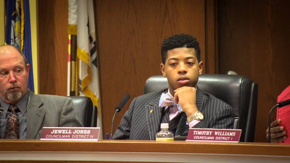 Jewell Jones sits, looking thoughtful, behind his name placard and next to other representatives.