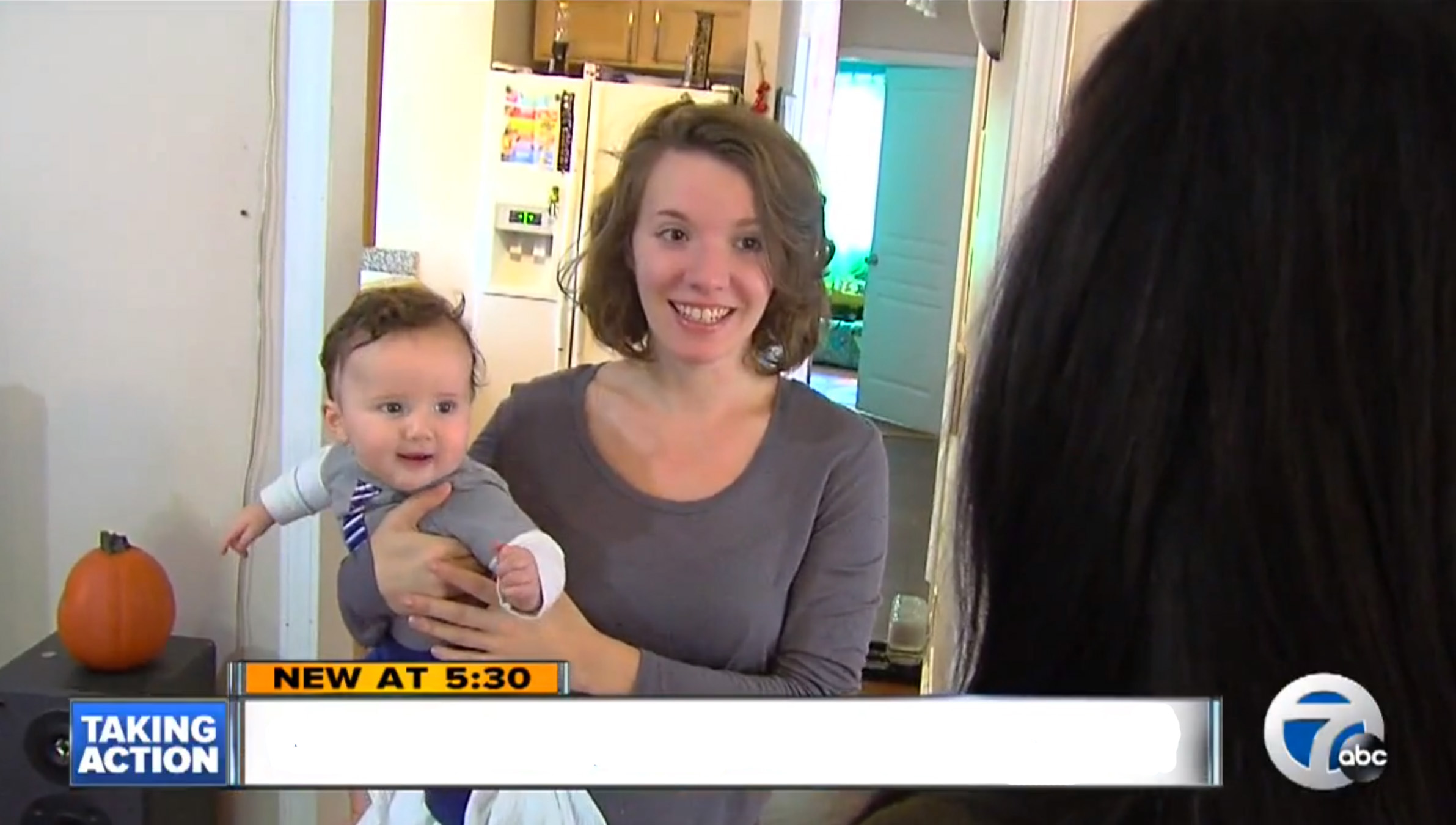 Ashley McPherson hold her son on her hip, standing in front of her kitchen and looking at a reporter.