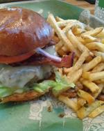 A large cheeseburger sits next to a pile of french fries.