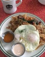 Top view of a plate of breakfast food, with several condiments. A mug of coffee sits next to the plate.