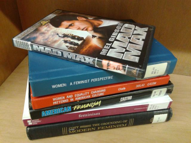 A stack of several feminist books with a DVD copy of the film "Mad Max" sitting on top.