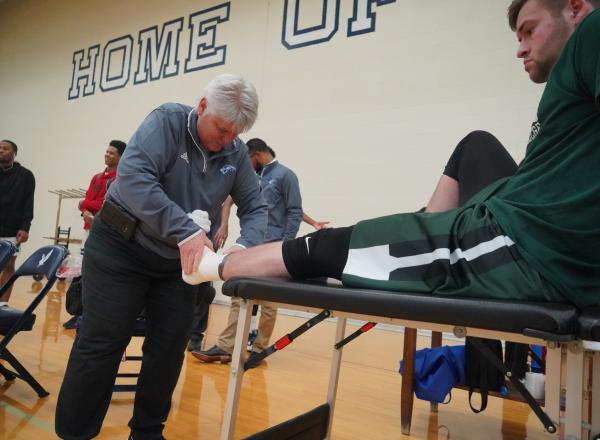 Jan Lauer HFC Athletic Trainer tending to athlete in gym, Henry Ford College main campus, Dearborn, MI photo courtesy Hawks Athletics