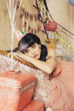 Melanie Martinez promotional photo wearing pink birthday dress with a birthday hat, but pouting.