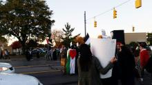 A row of protesters move across a street, holding signs and Palestinian flags.